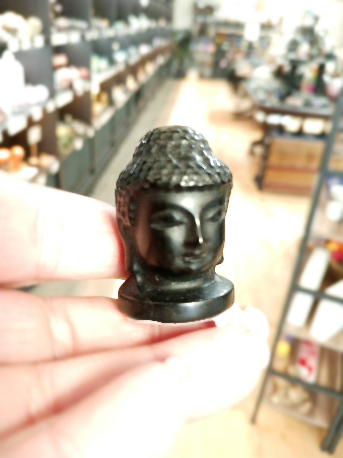 Hand-carved 1 1/2 inch tall Buddha head figurines in assorted crystal materials such as amethyst, rose quartz, clear quartz, and jade, displayed on a white background.