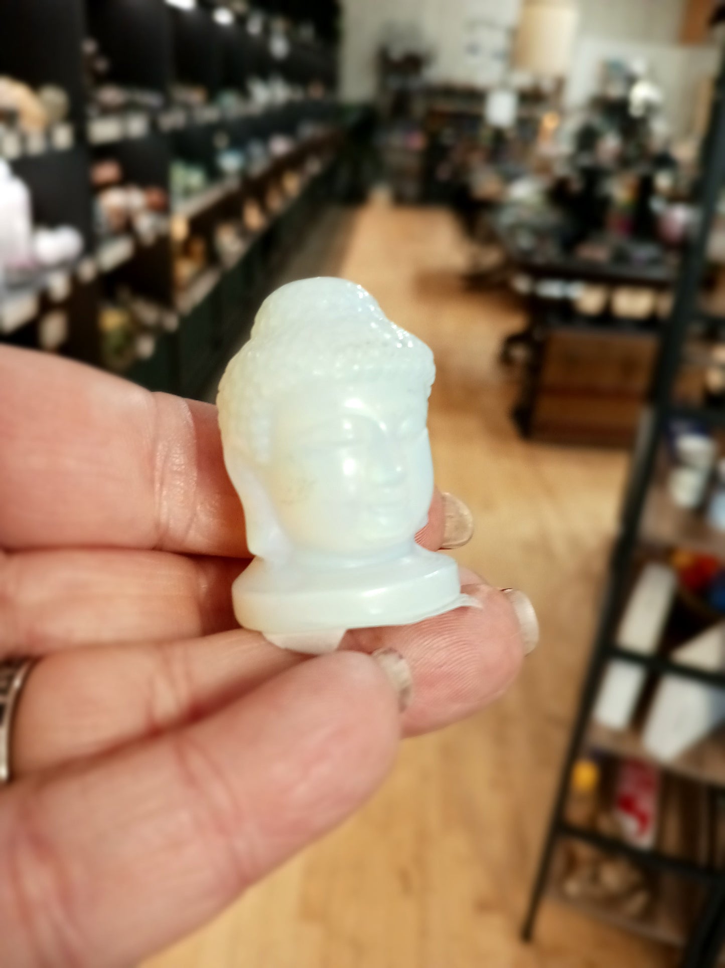 Hand-carved 1 1/2 inch tall Buddha head figurines in assorted crystal materials such as amethyst, rose quartz, clear quartz, and jade, displayed on a white background.