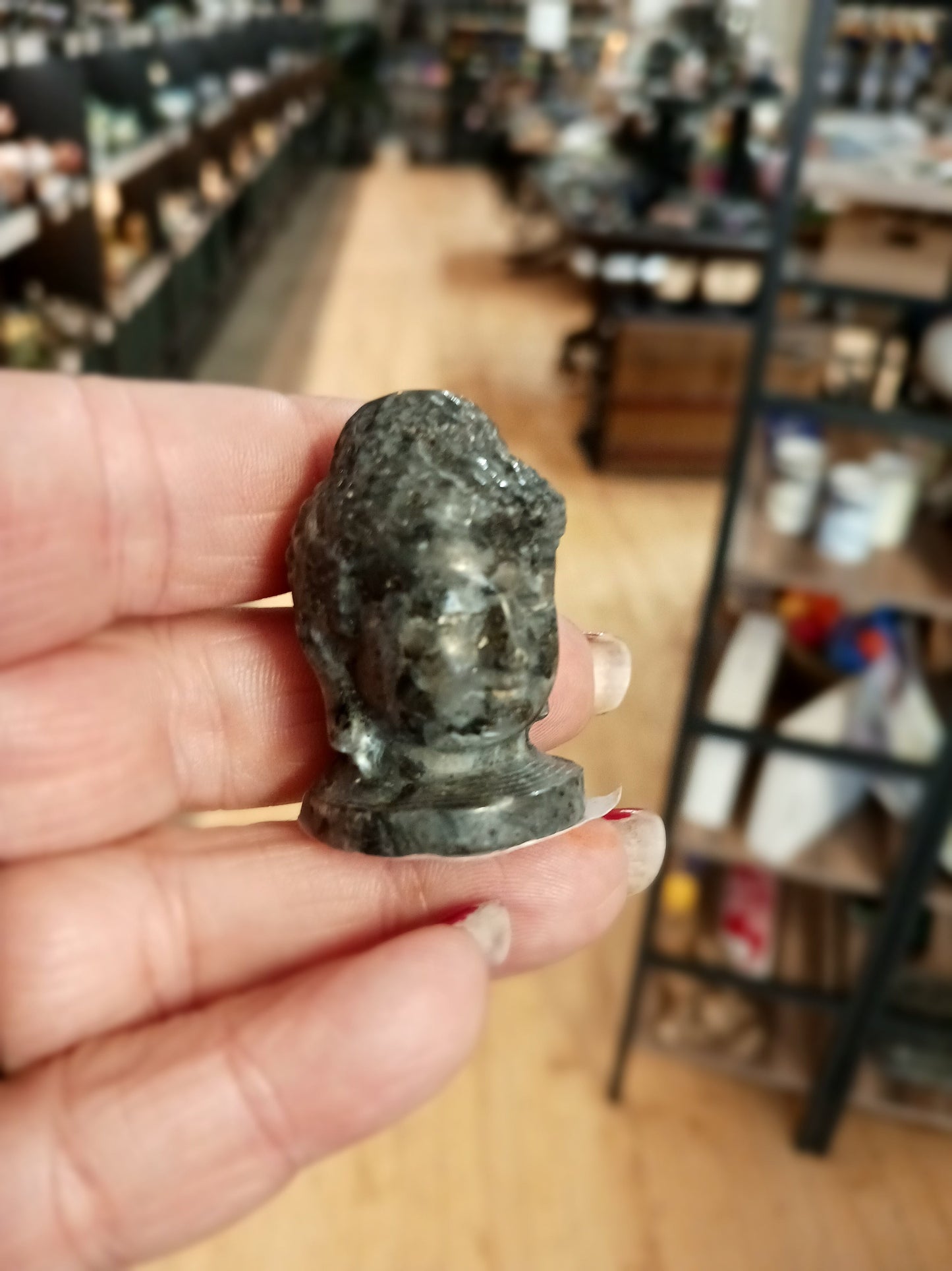Hand-carved 1 1/2 inch tall Buddha head figurines in assorted crystal materials such as amethyst, rose quartz, clear quartz, and jade, displayed on a white background.