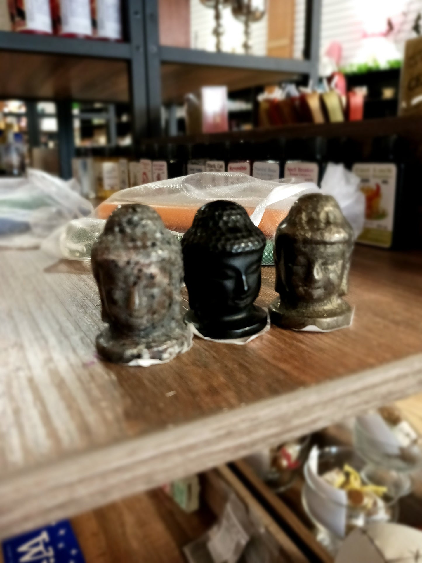 Hand-carved 1 1/2 inch tall Buddha head figurines in assorted crystal materials such as amethyst, rose quartz, clear quartz, and jade, displayed on a white background.