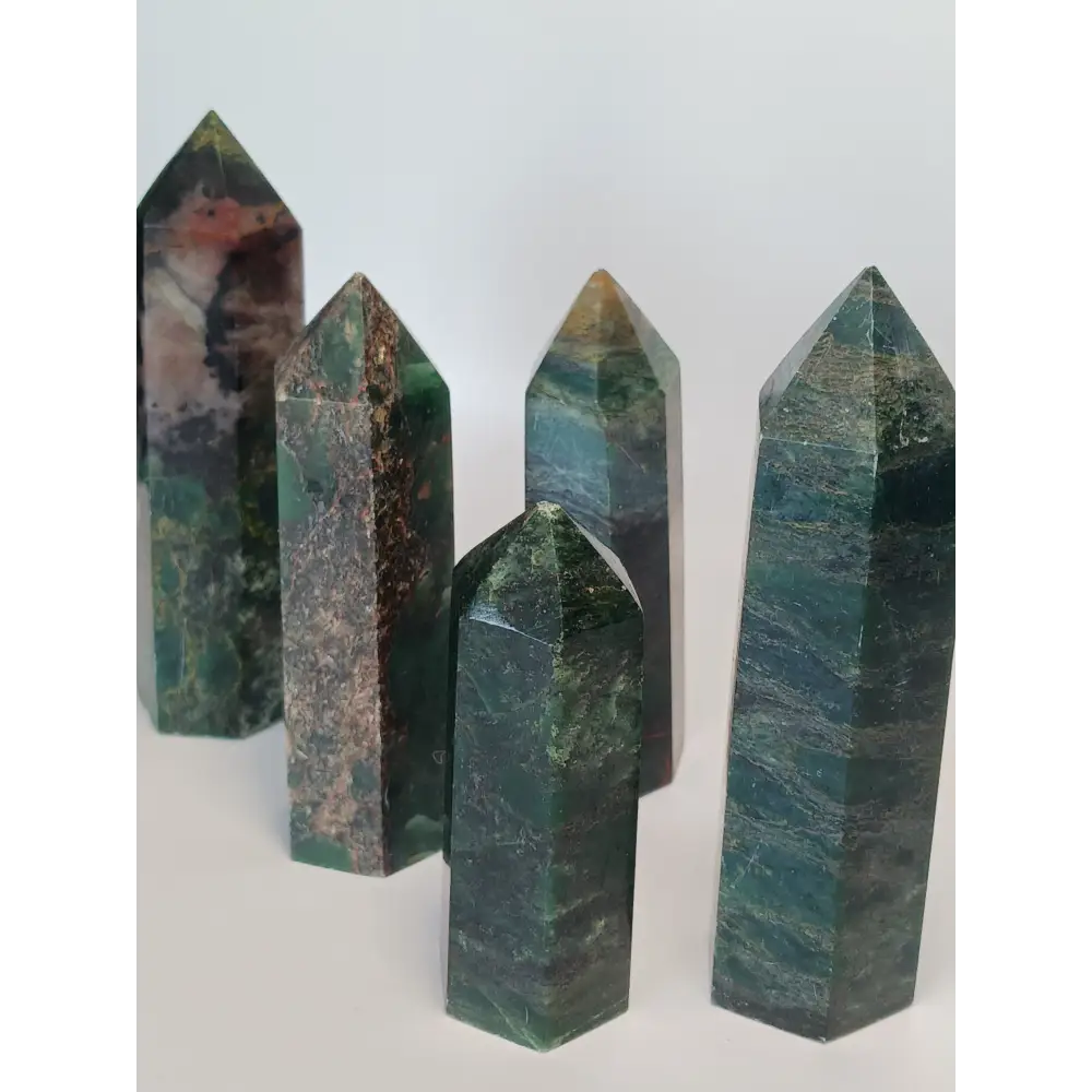 Hand-polished Green Zoisite stone featuring vibrant green hues, sometimes with black or ruby inclusions, displayed on a white background.