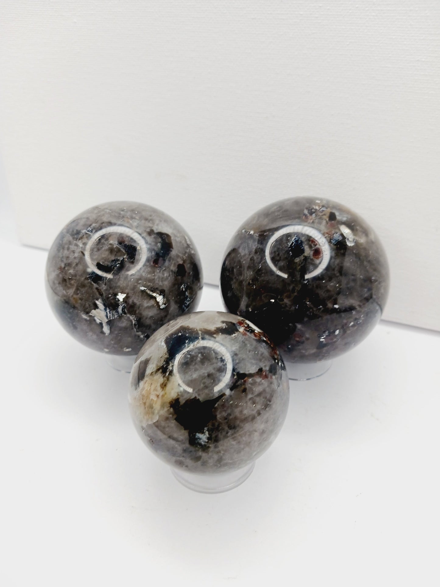 Quartz, garnet, tourmaline, and mica sphere, polished with clear, red, black, and shimmering inclusions, displayed on a white background.