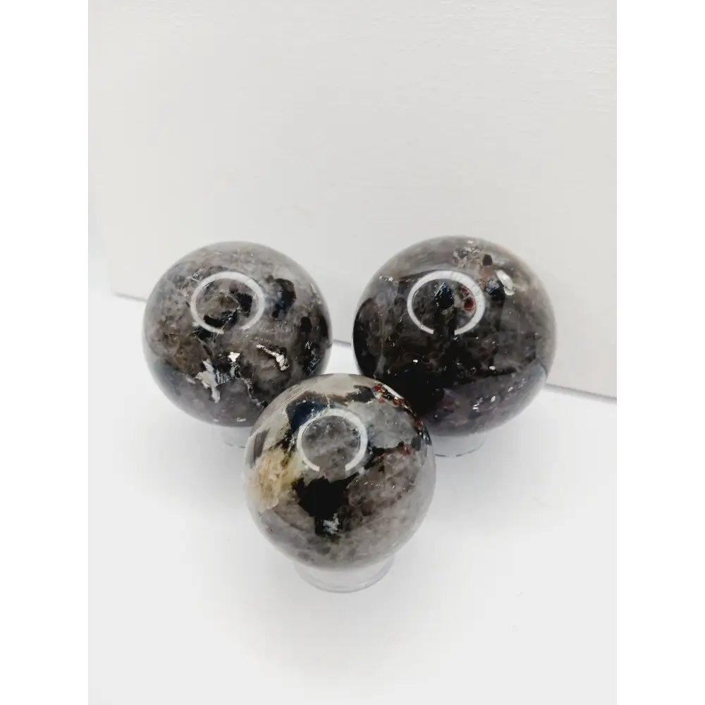Quartz, garnet, tourmaline, and mica sphere, polished with clear, red, black, and shimmering inclusions, displayed on a white background.