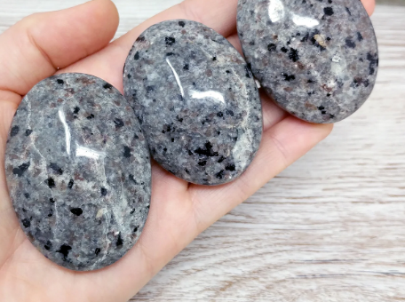 Hand-polished Yooperlite palmstone, glowing with vibrant orange and yellow patterns under UV light, displayed on a white background. Perfect for creativity, transformation, and mystical energy.