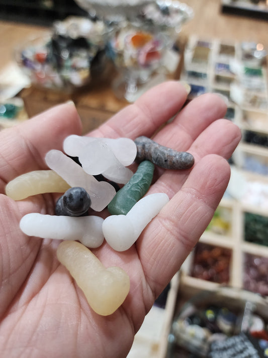 Assorted 1 inch penis-shaped crystal carvings in various colors and stones, hand-carved and displayed on a white background. Perfect for playful energy, empowerment, and root chakra healing.