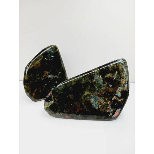 Labradorite freeform with vibrant flashes of blue, green, and gold, polished and displayed on a white background.