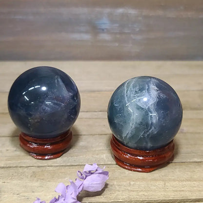 Hand-polished Blue Rose Quartz sphere, 1.5 to 1.75 inches in diameter, featuring soothing blue and soft pink hues, displayed on a white background.