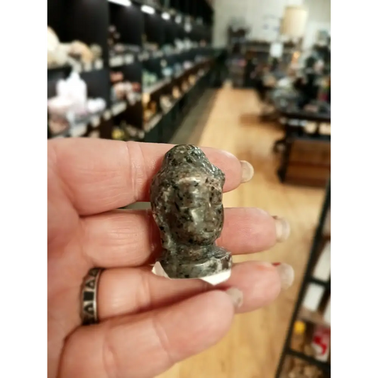 Hand-carved 1 1/2 inch tall Buddha head figurines in assorted crystal materials such as amethyst, rose quartz, clear quartz, and jade, displayed on a white background.