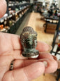 Hand-carved 1 1/2 inch tall Buddha head figurines in assorted crystal materials such as amethyst, rose quartz, clear quartz, and jade, displayed on a white background.