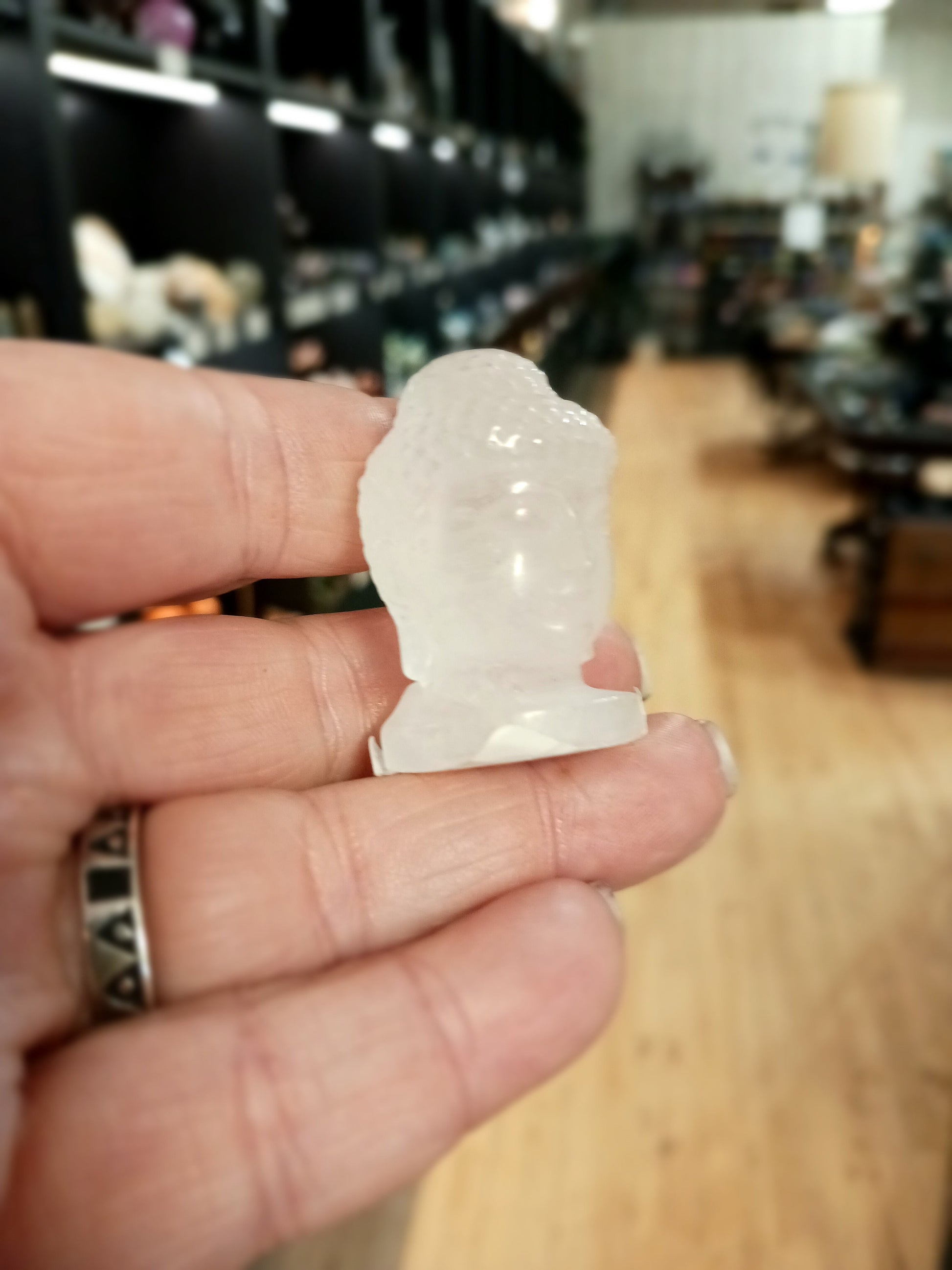 Hand-carved 1 1/2 inch tall Buddha head figurines in assorted crystal materials such as amethyst, rose quartz, clear quartz, and jade, displayed on a white background.