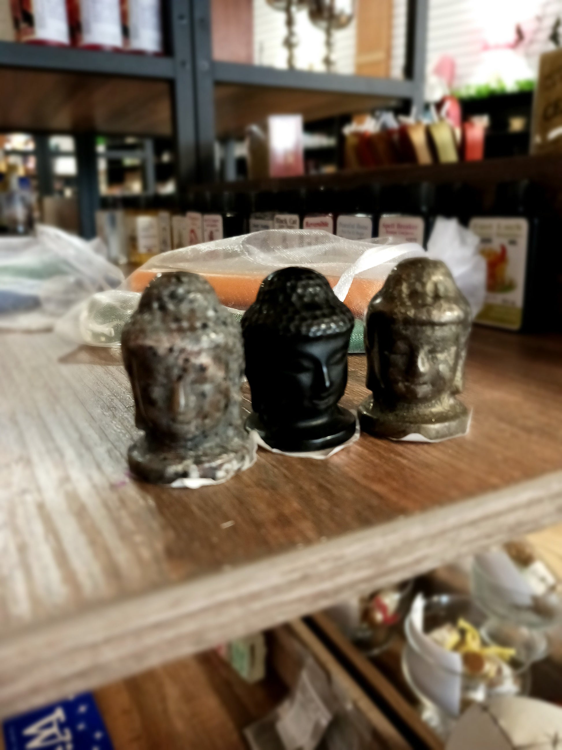 Hand-carved 1 1/2 inch tall Buddha head figurines in assorted crystal materials such as amethyst, rose quartz, clear quartz, and jade, displayed on a white background.