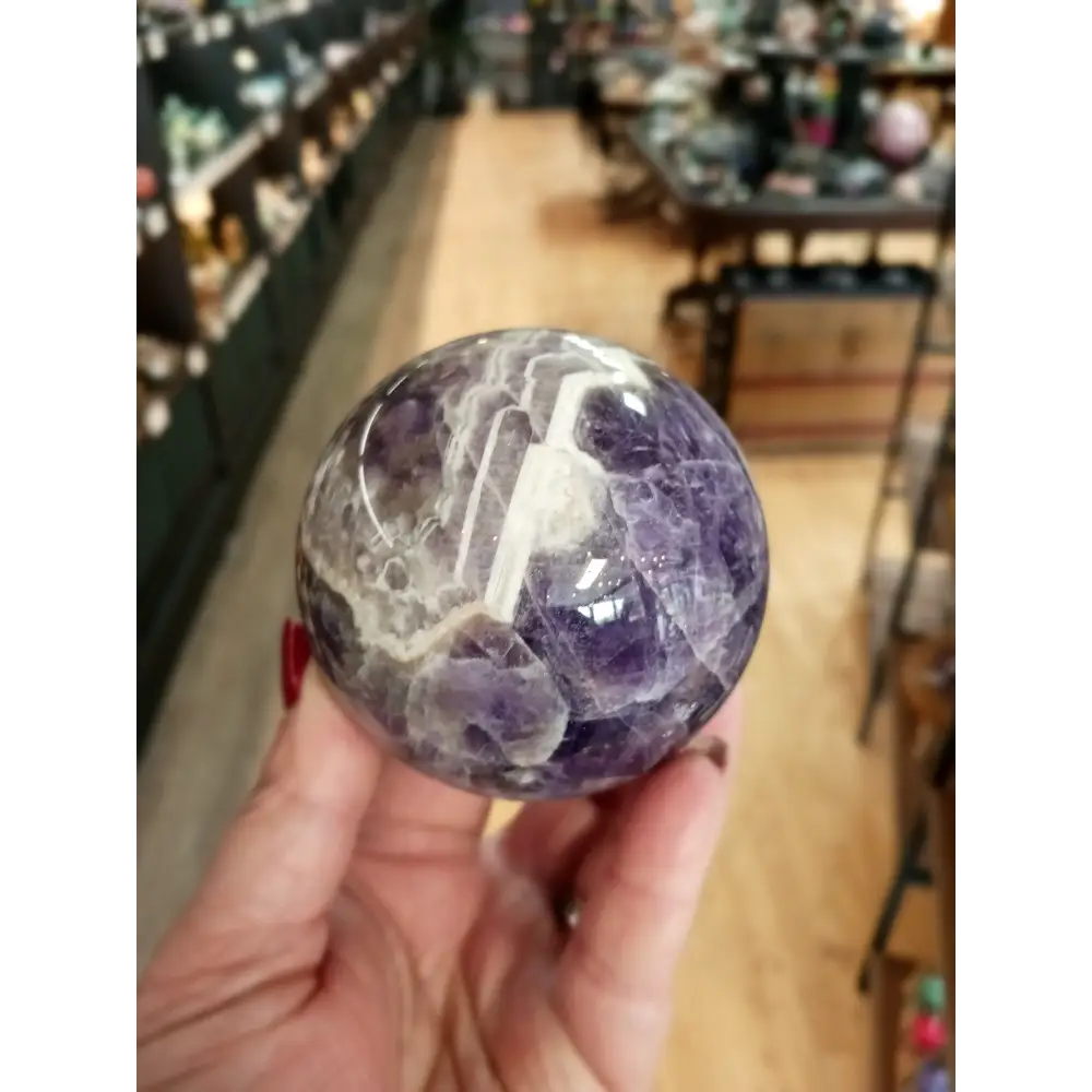 Hand-polished Dream Amethyst sphere featuring vivid purple and white chevron bands, displayed on a white background.
