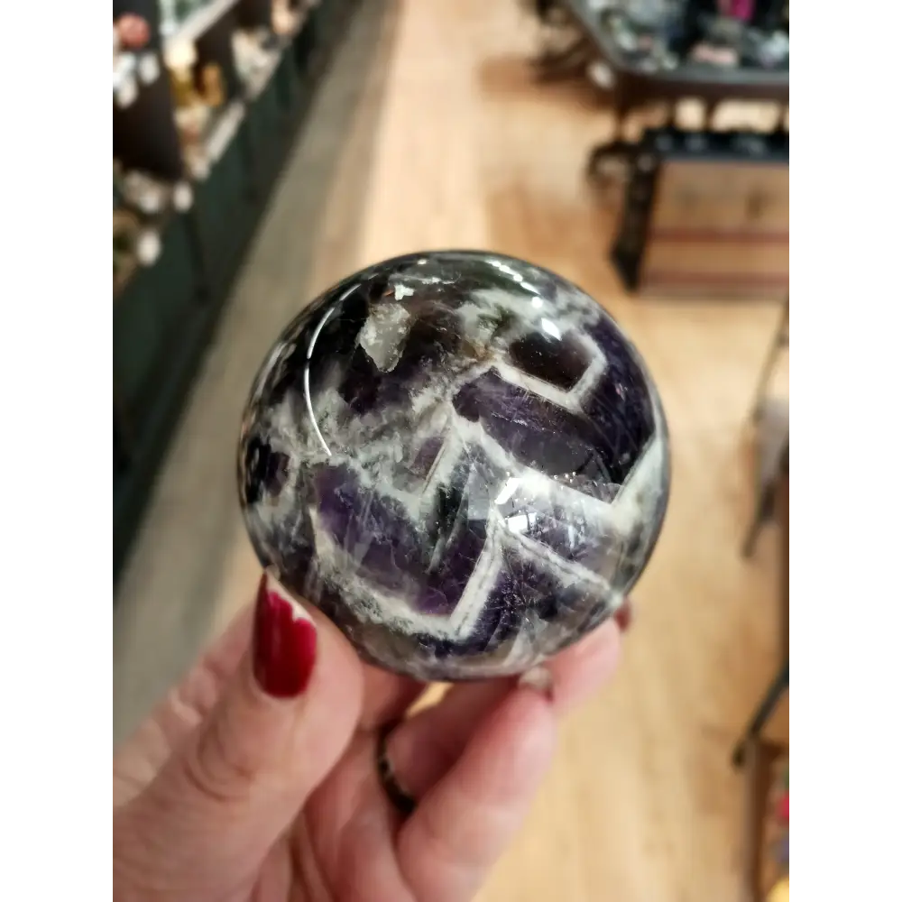 Hand-polished Dream Amethyst sphere featuring vivid purple and white chevron bands, displayed on a white background.