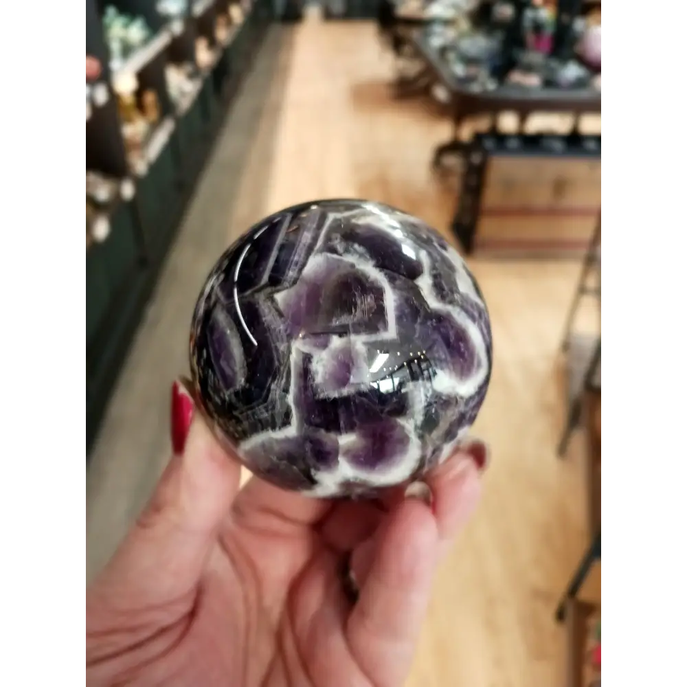 Hand-polished Dream Amethyst sphere featuring vivid purple and white chevron bands, displayed on a white background.