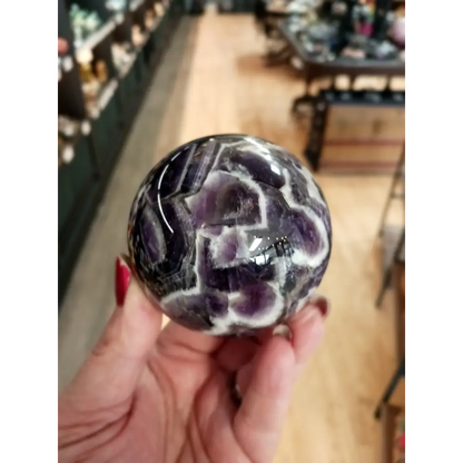 Hand-polished Dream Amethyst sphere featuring vivid purple and white chevron bands, displayed on a white background.