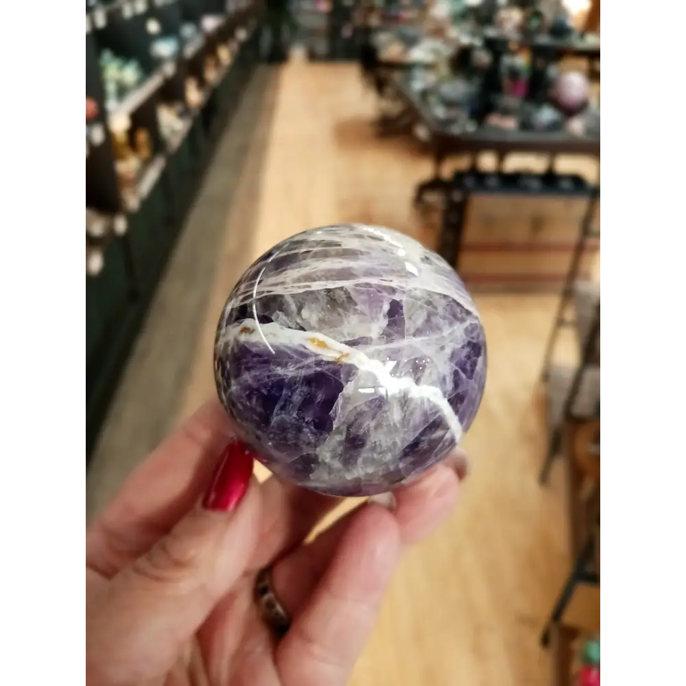 Hand-polished Dream Amethyst sphere featuring vivid purple and white chevron bands, displayed on a white background.