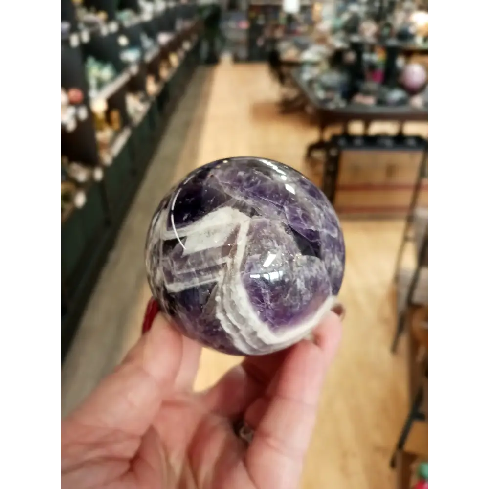 Hand-polished Dream Amethyst sphere featuring vivid purple and white chevron bands, displayed on a white background.