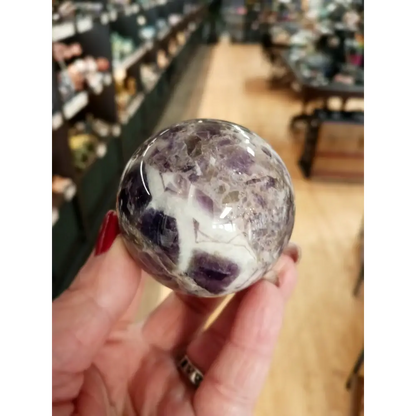 Hand-polished Dream Amethyst sphere featuring vivid purple and white chevron bands, displayed on a white background.