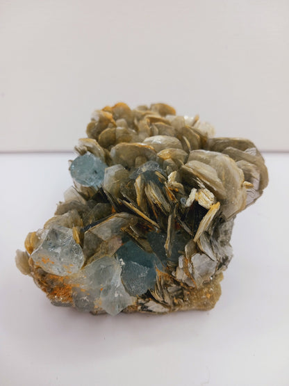 Muscovite with aquamarine specimen, showcasing shimmering layers and blue crystal accents, displayed on a white background.