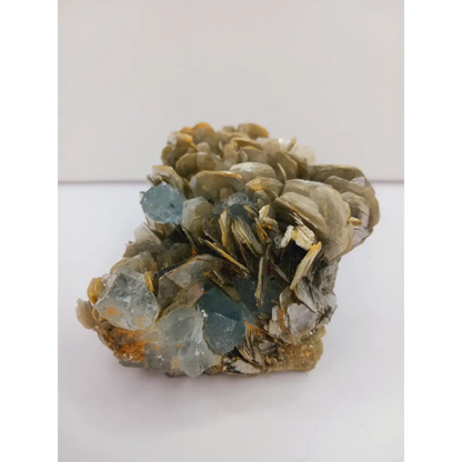 Muscovite with aquamarine specimen, showcasing shimmering layers and blue crystal accents, displayed on a white background.
