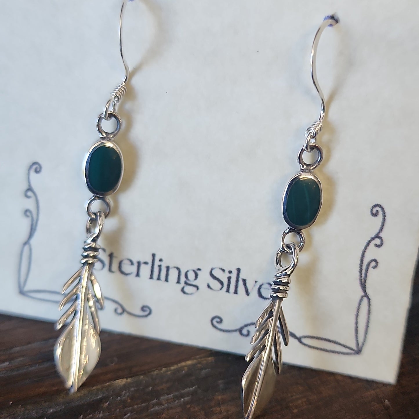 Sterling silver feather earrings featuring vibrant malachite stones, displayed on a white background. Perfect for transformation, protection, and spiritual freedom.