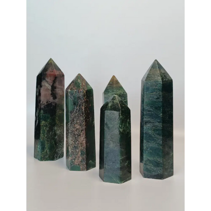 Hand-polished Green Zoisite stone featuring vibrant green hues, sometimes with black or ruby inclusions, displayed on a white background.