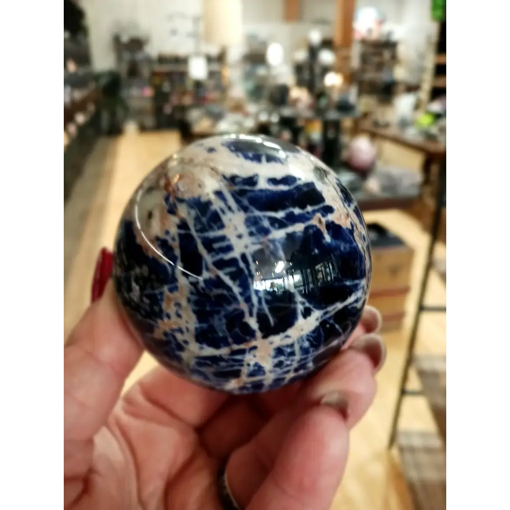 Hand-polished Sodalite sphere featuring deep blue hues with natural white marbling, displayed on a white background.