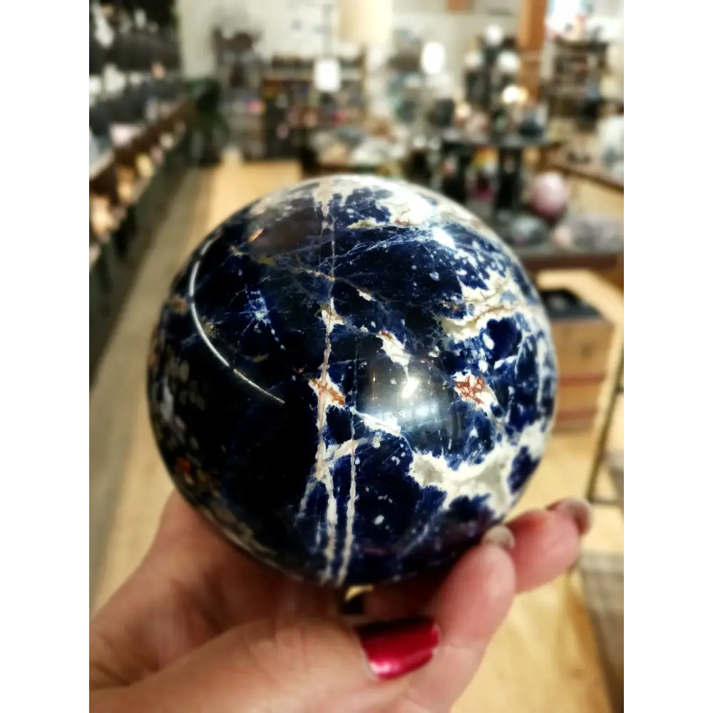 Hand-polished Sodalite sphere featuring deep blue hues with natural white marbling, displayed on a white background.