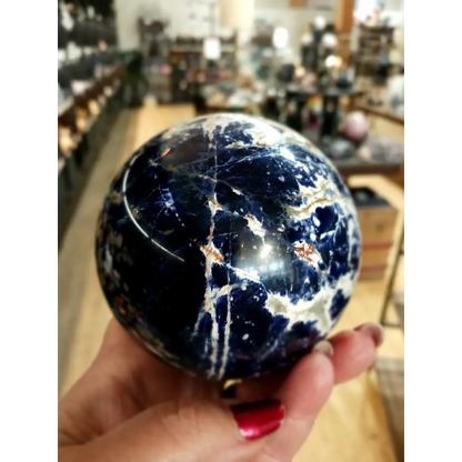 Hand-polished Sodalite sphere featuring deep blue hues with natural white marbling, displayed on a white background.