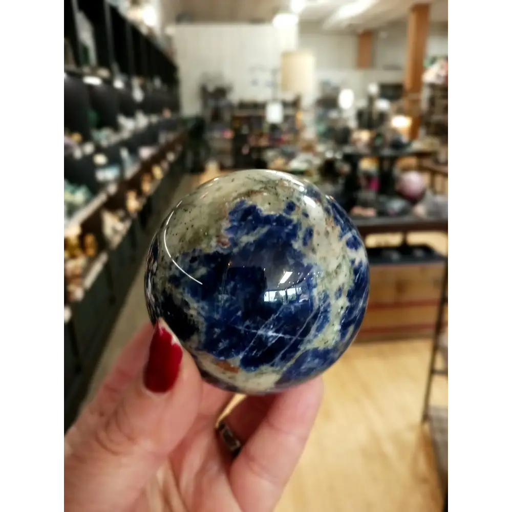 Hand-polished Sodalite sphere featuring deep blue hues with natural white marbling, displayed on a white background.