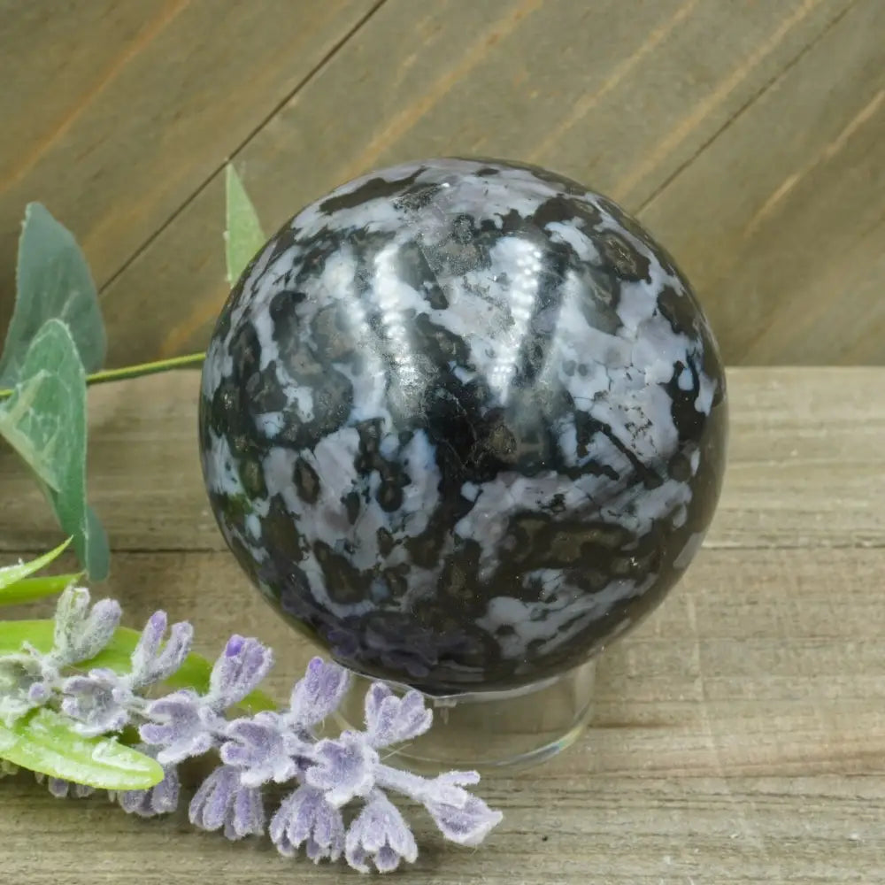 Hand-polished Indigo Gabbro sphere featuring swirling indigo, black, and gray patterns, displayed on a white background.
