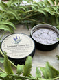 Lavender Lotion Bar in a round shape, surrounded by sprigs of fresh lavender and natural butters, displayed on a white background. Perfect for nourishing, soothing, and hydrating skin.