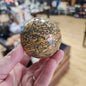 Hand-polished Leopard Skin Jasper sphere featuring bold, spotted patterns in earthy tones, displayed on a white background.