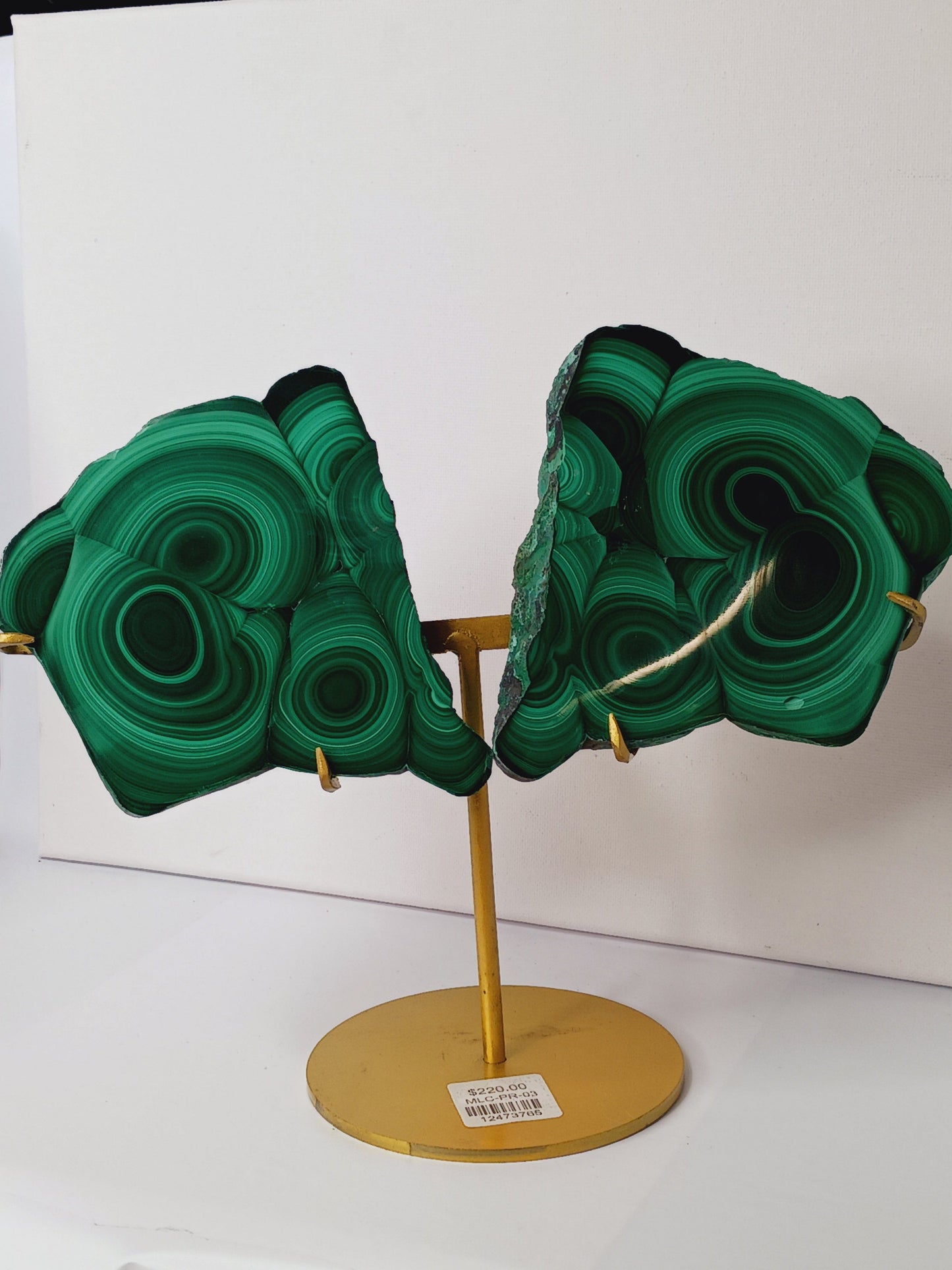 Pair of polished malachite slabs with vibrant green banding, displayed upright on a metal stand against a white background.