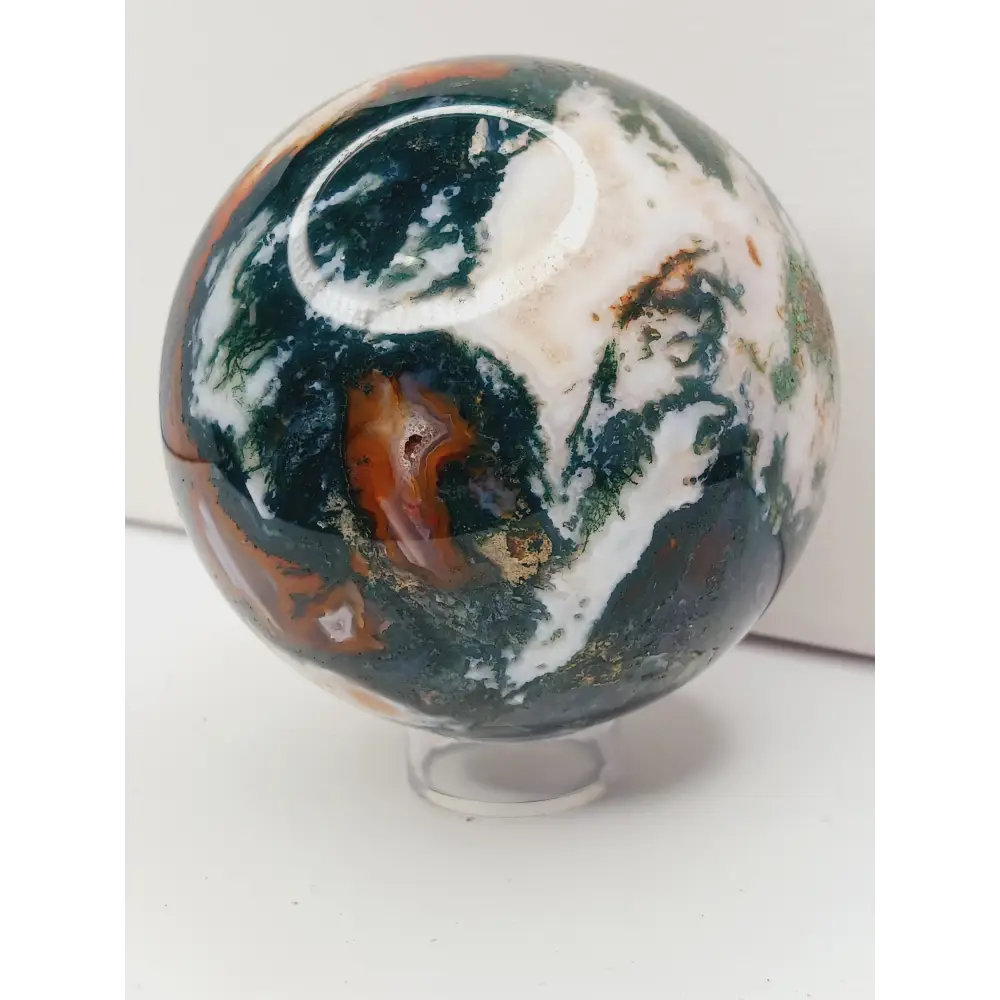 Moss Agate sphere with deep green swirls and sparkling druzy pocket, displayed on a white background.