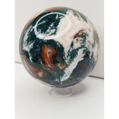 Moss Agate sphere with deep green swirls and sparkling druzy pocket, displayed on a white background.