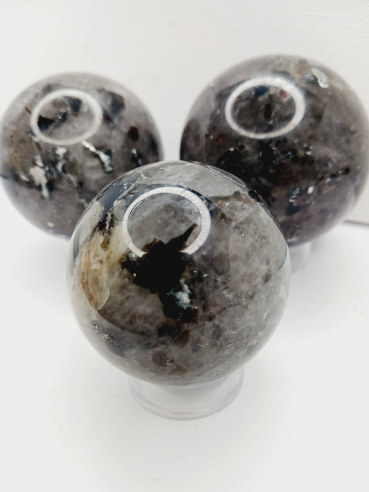 Quartz, garnet, tourmaline, and mica sphere, polished with clear, red, black, and shimmering inclusions, displayed on a white background.