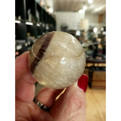 Hand-polished Rainbow and Clear Fluorite sphere featuring luminous bands of purple, green, blue, and clear tones, displayed on a white background.