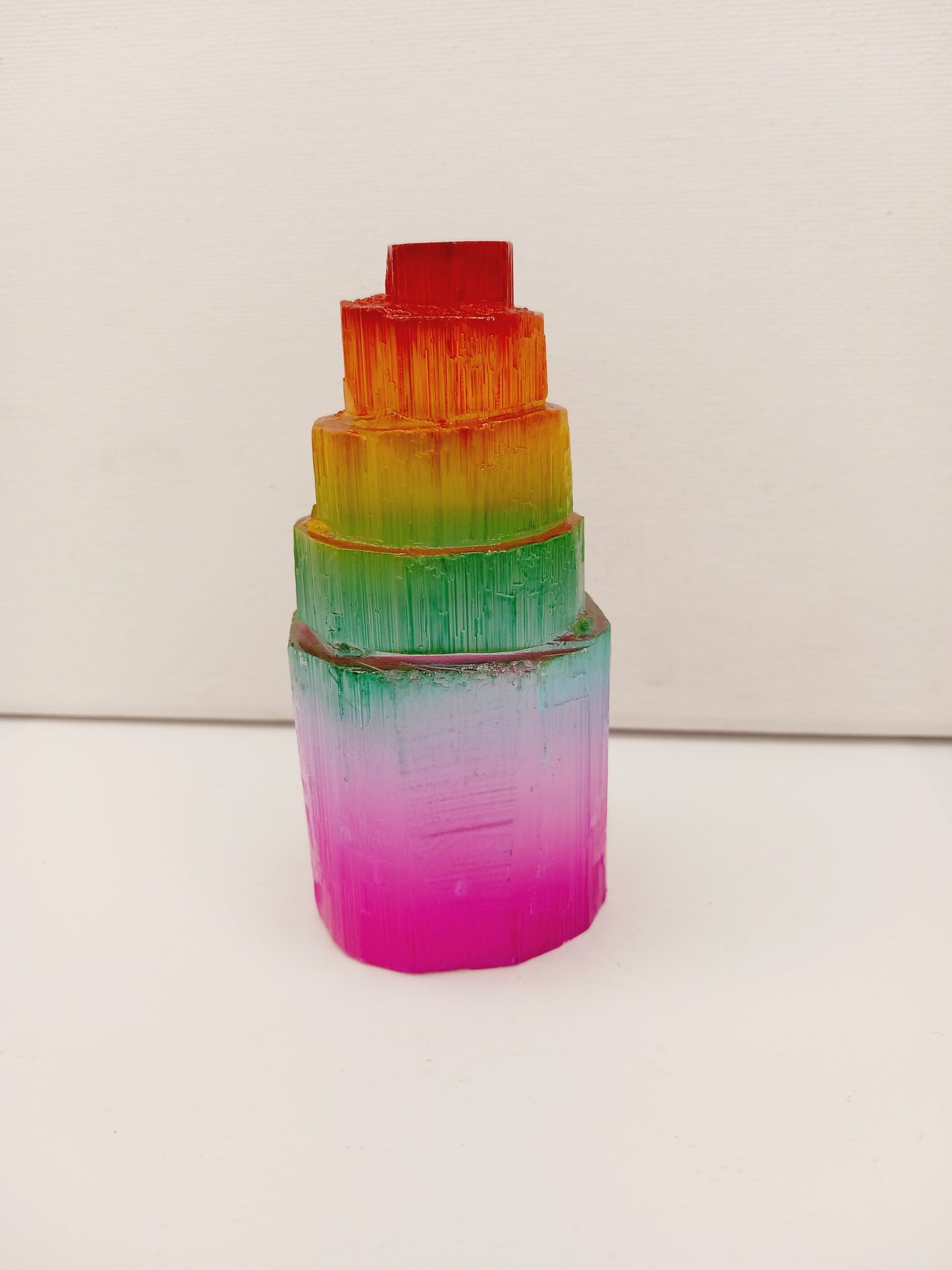 Rainbow selenite tiered tower, polished with a vibrant rainbow sheen and step-like design, displayed on a white background.