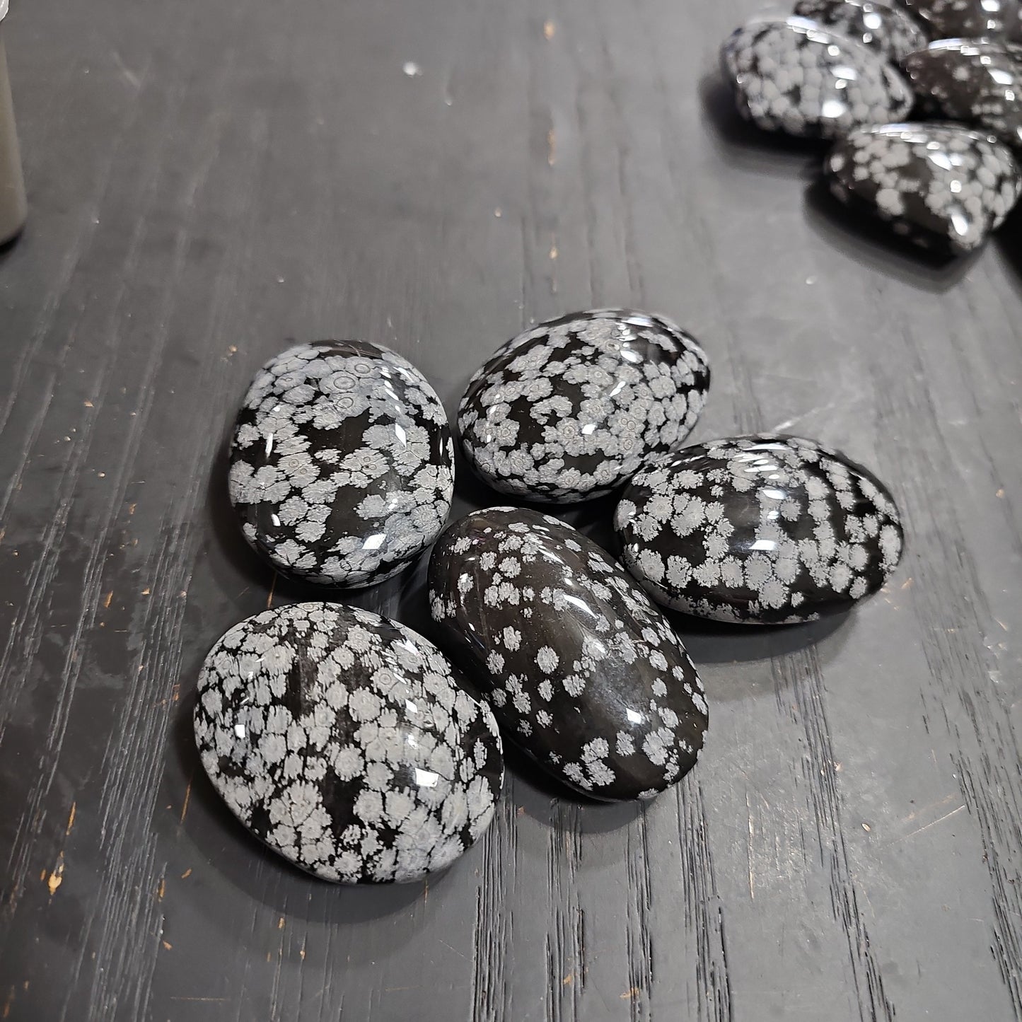 Hand-polished snowflake obsidian hearts and palmstones, featuring black stone with white snowflake patterns, displayed on a white background. Perfect for grounding, protection, and gentle transformation.