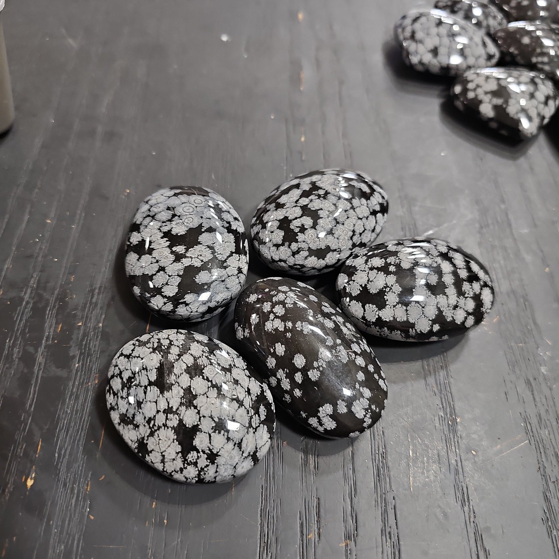 Hand-polished snowflake obsidian hearts and palmstones, featuring black stone with white snowflake patterns, displayed on a white background. Perfect for grounding, protection, and gentle transformation.
