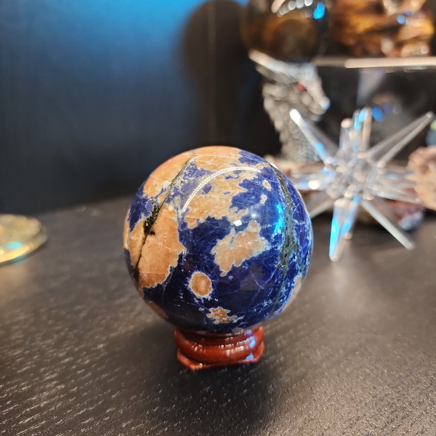 Hand-polished Sunset Sodalite sphere featuring vibrant blue sodalite with glowing orange sunstone streaks, displayed on a white background.