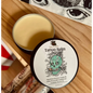 Tattoo Healing Balm in a small jar, surrounded by fresh herbs and natural oils, displayed on a white background. Perfect for soothing, protecting, and revitalizing tattoos.

