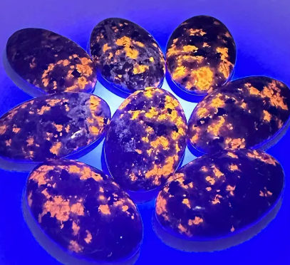 Hand-polished Yooperlite palmstone, glowing with vibrant orange and yellow patterns under UV light, displayed on a white background. Perfect for creativity, transformation, and mystical energy.